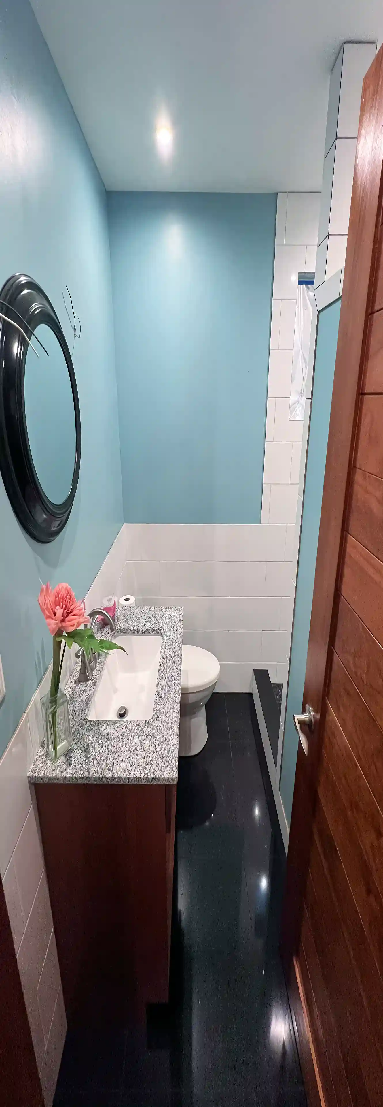 View into the bathroom showing black tile floor, white tile...